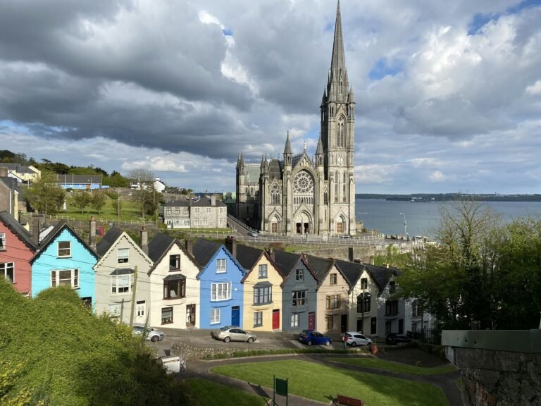 Gothic architecture of St. Colman's Cathedral against a vibrant row of houses in Cobh, Ireland by the sea.